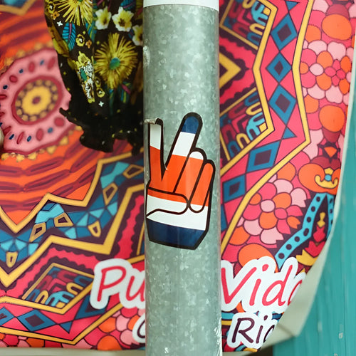 A vibrant orange white and blue peace sign sticker on a textured metallic pole with candido c41 color 400 iso 35mm color negative film