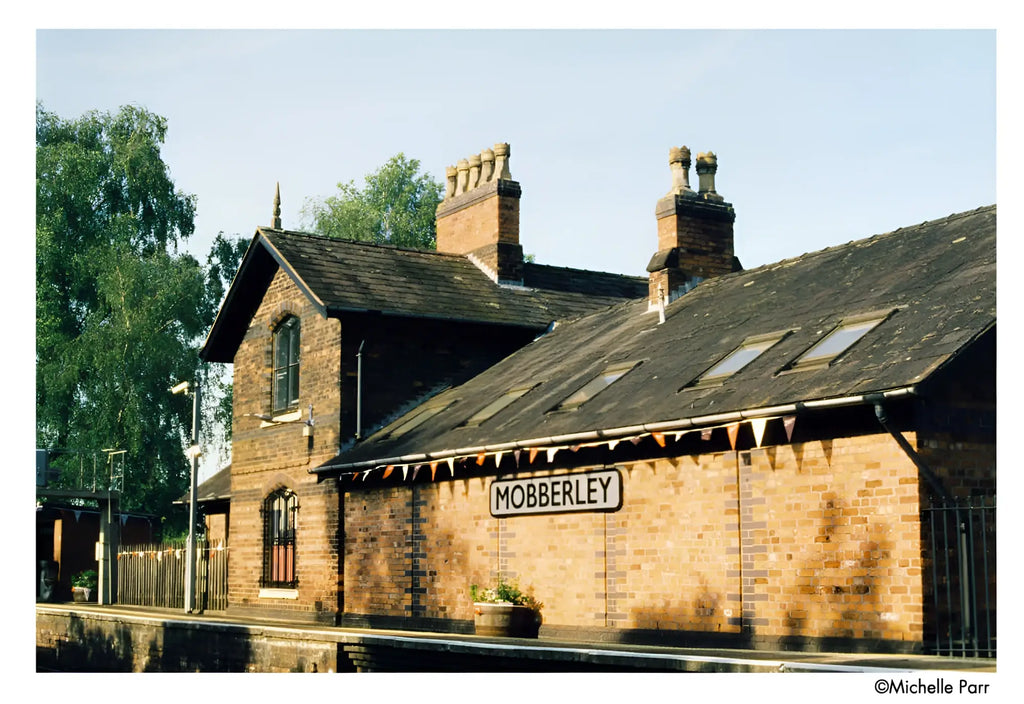 The sign reads ’mobberley’ in black uppercase letters on a white rectangular background, mounted centrally above the station entrance.