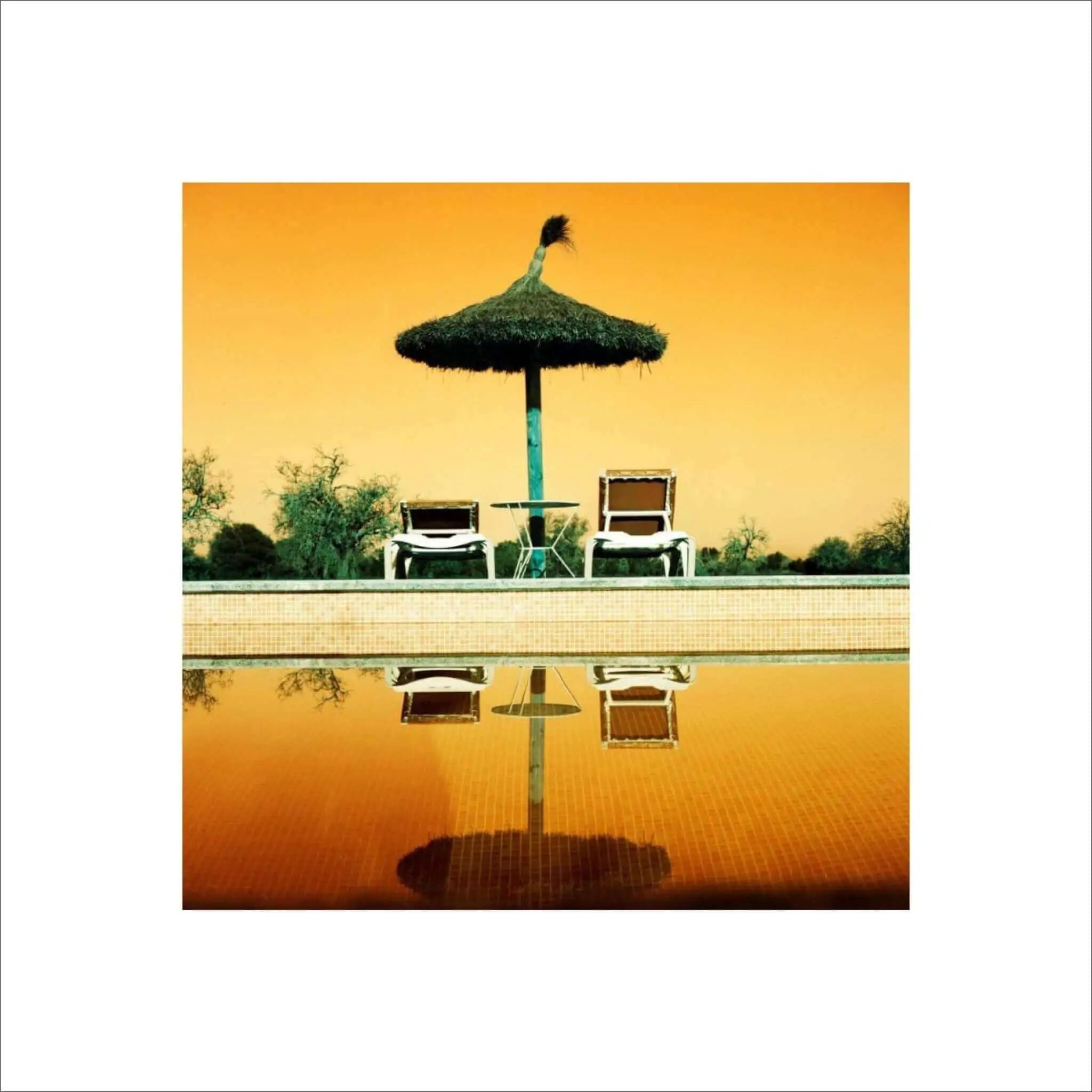 A thatched umbrella with a green pole stands beside two white lounge chairs by the poolside.